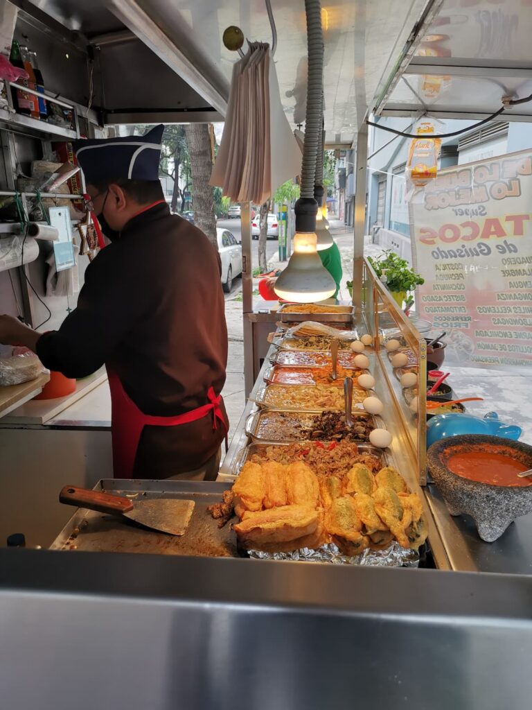 Street taco guisado stand in Mexico City with rows of fillings under heat lamps