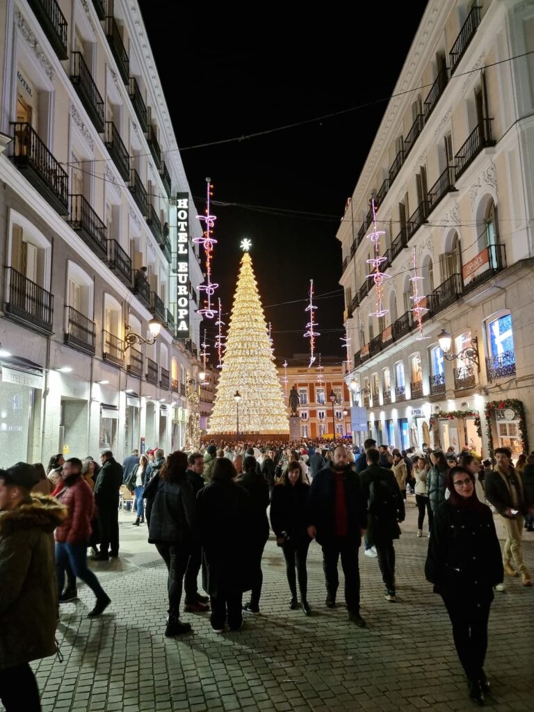 Crowds of locals on Calle del Carmen during Christmas in Madrid, with the Sol tree glowing at the end of the street