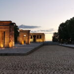 Templo de Debod lit at dusk in Madrid, with warm sunset sky and cobblestone foreground