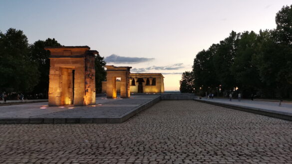 Templo de Debod lit at dusk in Madrid, with warm sunset sky and cobblestone foreground