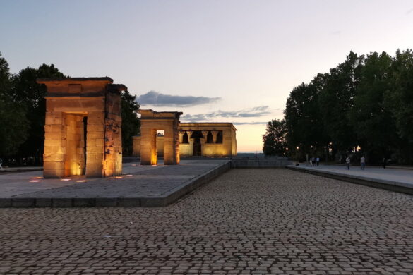 Templo de Debod lit at dusk in Madrid, with warm sunset sky and cobblestone foreground