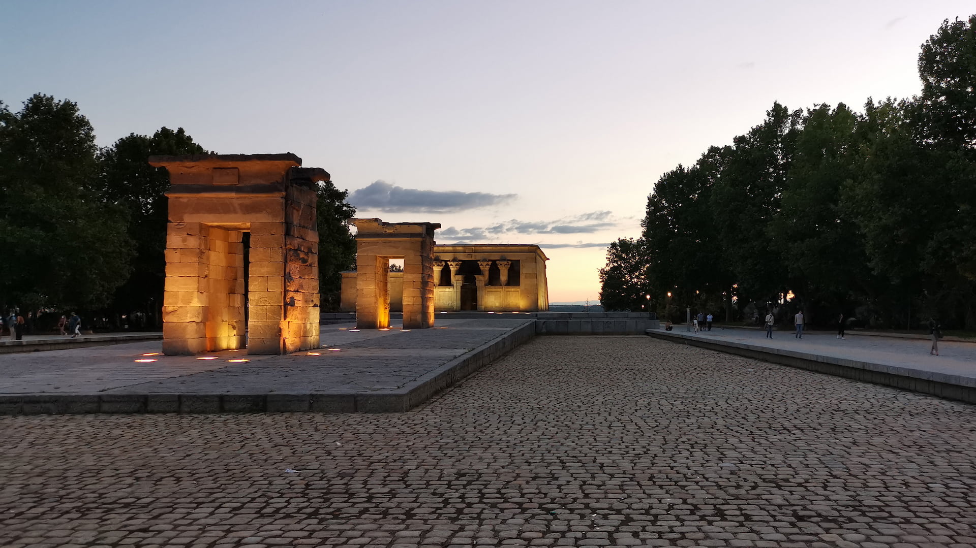 Templo de Debod lit at dusk in Madrid, with warm sunset sky and cobblestone foreground